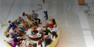 A team of people sitting around a circular sofa.